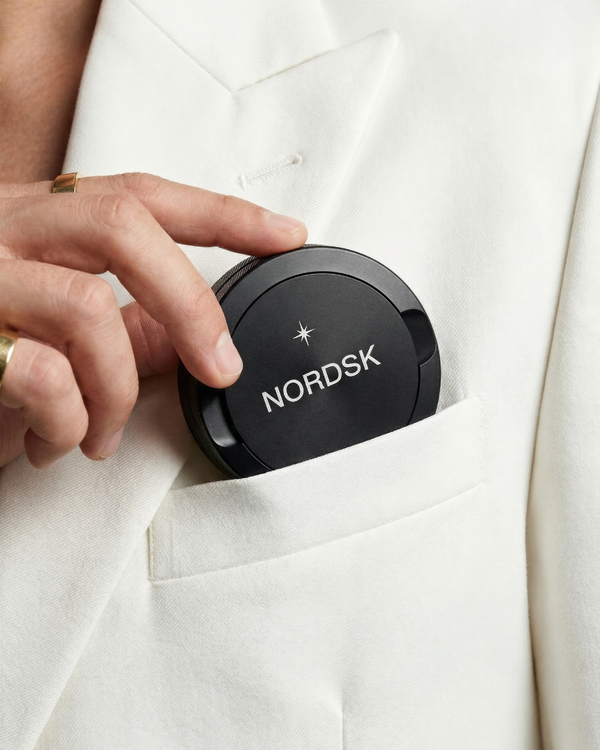 Person placing a black NORDSK snusdosa and nicotine container into a white pocket