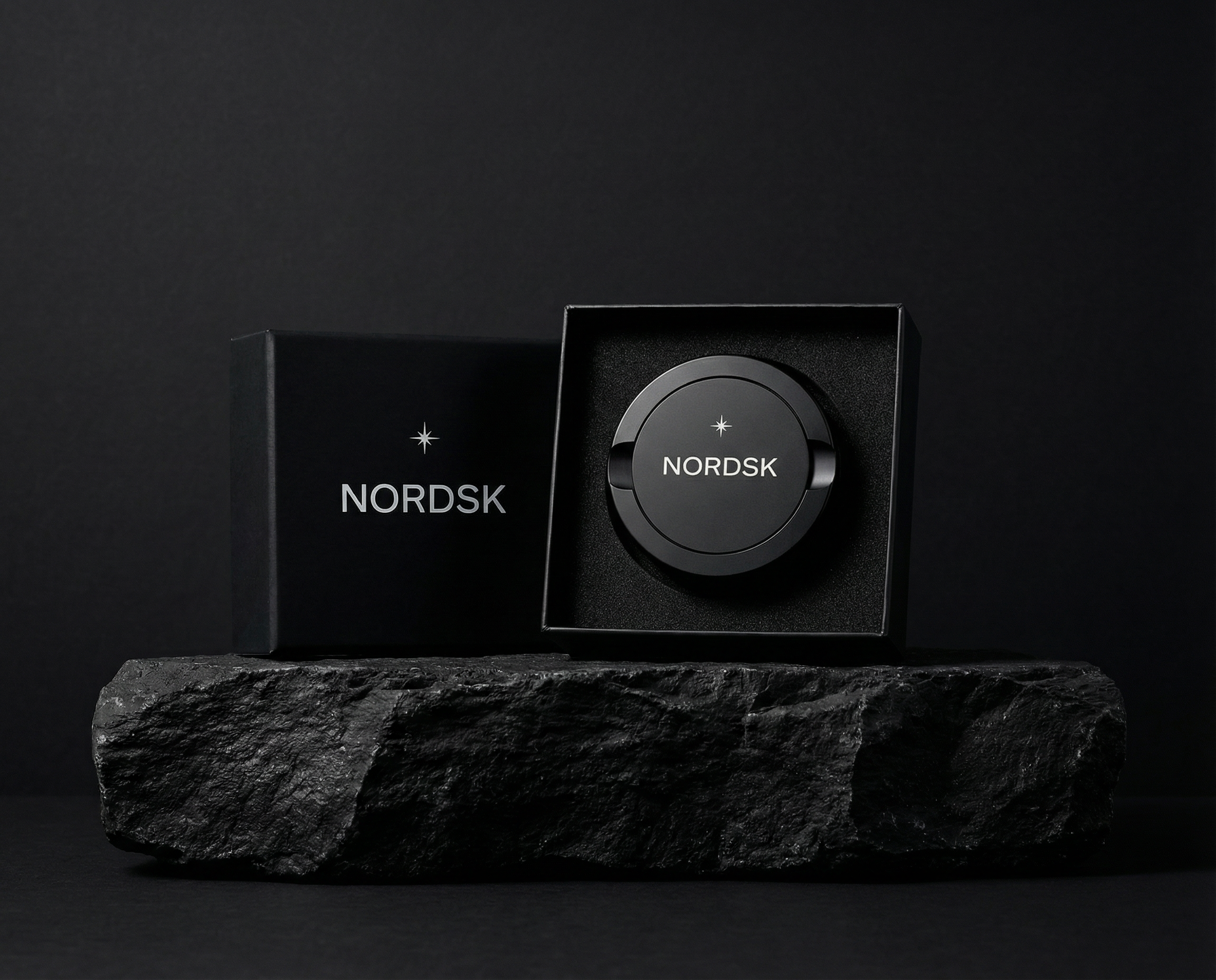 Black NORDSK snus tin and nicotine pouch container and box on a dark stone surface with a black background