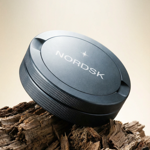 Grey NORDSK metal snus tin on a wooden surface with a neutral background. Designed in Sweden.