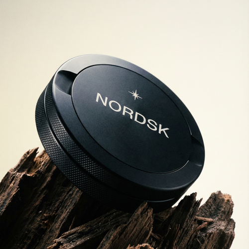 Black NORDSK metal snus tin on a wooden surface with a neutral background. Designed in Sweden.