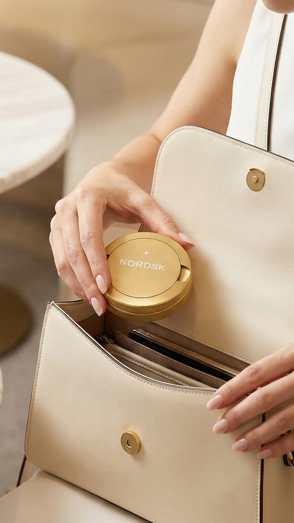 woman placing NORDSK snus tin into handbag. Light dress and beige handbag. Designed in Sweden.